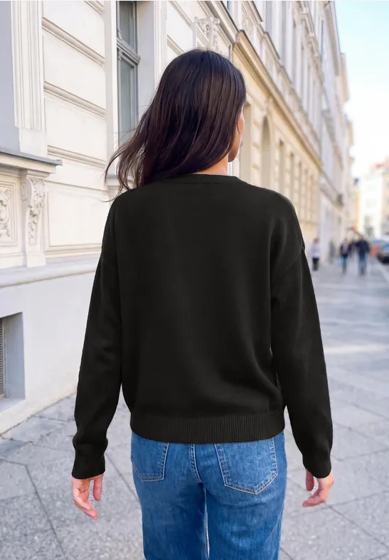 Frau von hinten in schwarzem Pullover und Jeans, stehend in einer europäischen Altstadtstraße.