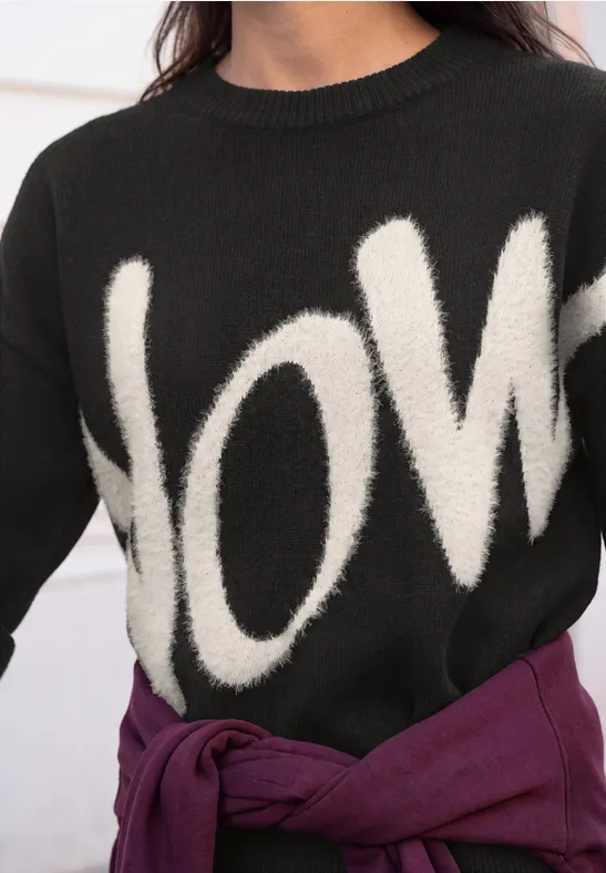 Schwarzer Pullover mit weißem Love-Schriftzug, lila Oberteil um die Taille gebunden.