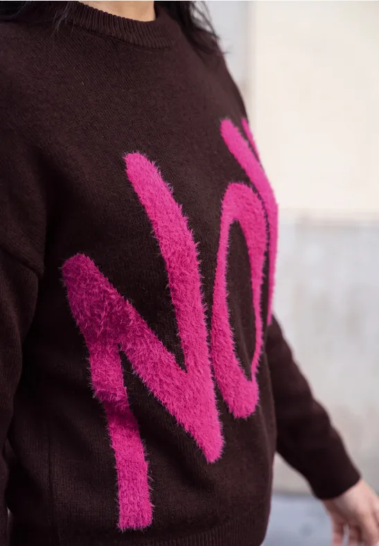 Person trägt braunen Pullover mit großem pinkfarbenem Schriftzug NO