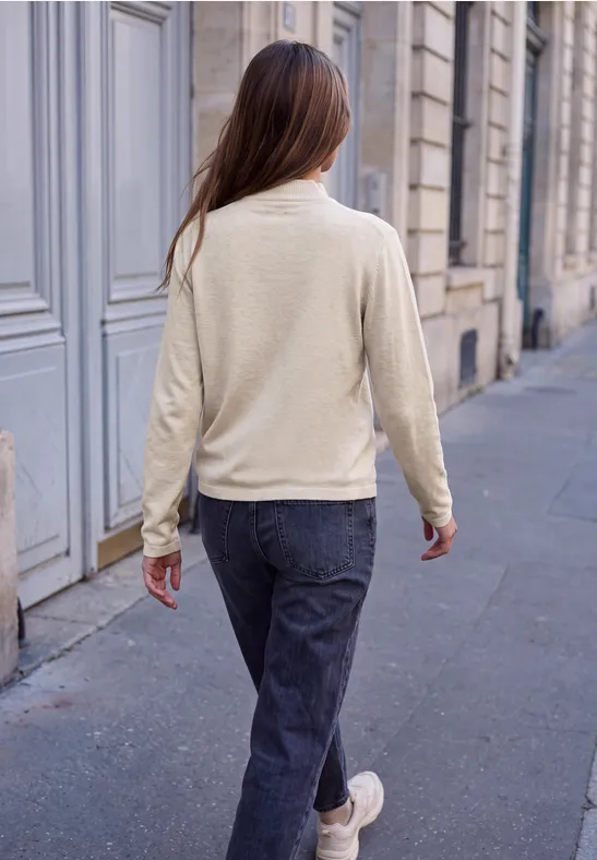 Frau mit beigem Pullover und Jeans, von hinten, läuft auf einer gepflasterten Straße.