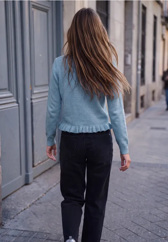Eine junge Frau mit langen Haaren in Jeansjacke und schwarzer Hose geht eine städtische Straße entlang.