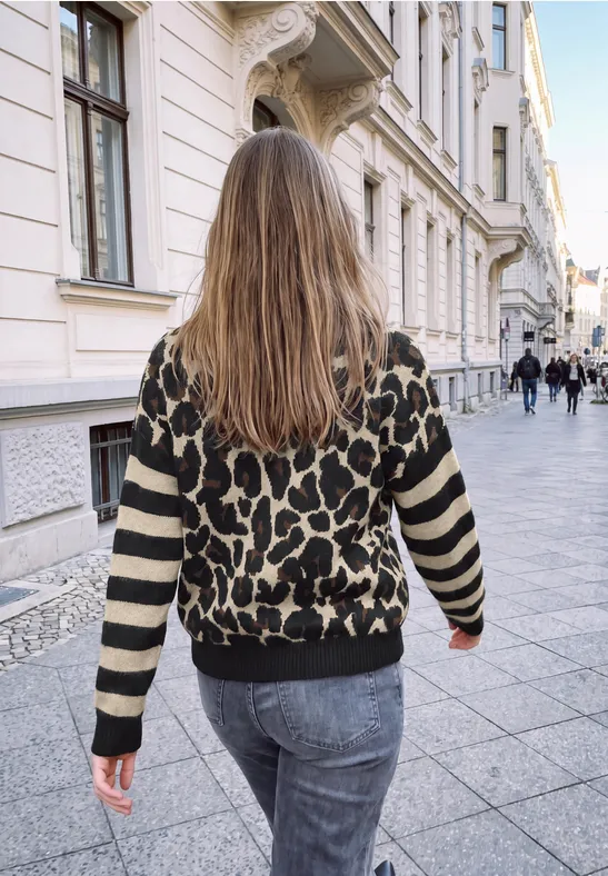 Frau mit langem Haar und Leopardenpullover spaziert durch eine elegante, städtische Gasse.