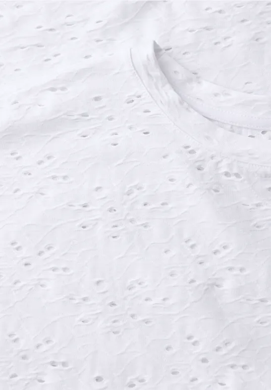 Close-up van wit opengewerkt textiel met fijn, gestructureerd borduurpatroon