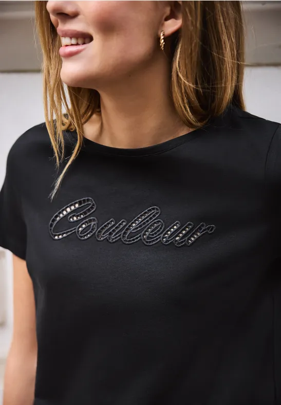 Vrouw draagt zwart t-shirt met strass-opdruk "Couleur".