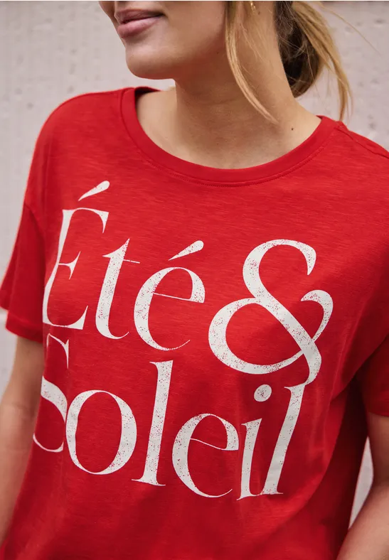 Vrouw draagt rood t-shirt met witte tekst 'Été & Soleil'