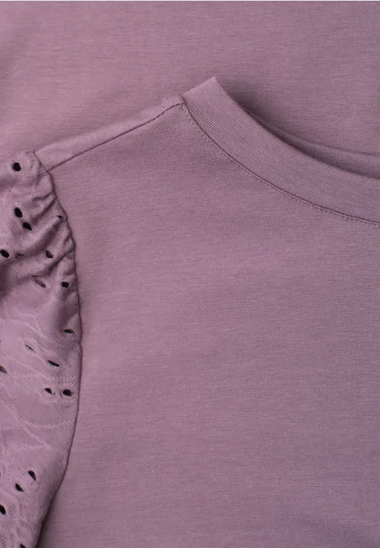Nahaufnahme eines violetten Shirts mit gerafftem Ärmel und dekorativen Cut-out-Details.
