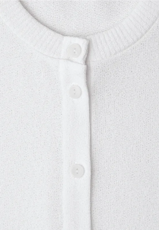 Gros plan d’un cardigan en maille blanc avec boutonnière.