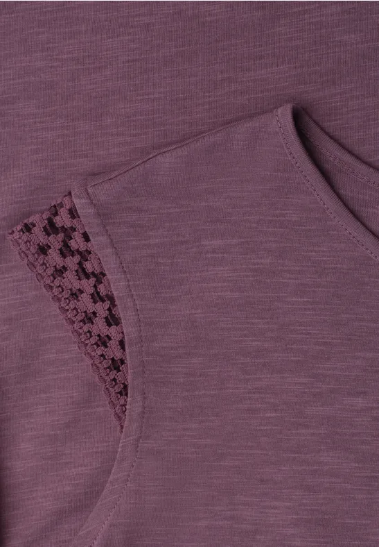 Nahaufnahme eines ärmellosen violetten Oberteils mit feinem Lochmuster-Einsatz an der Schulter.