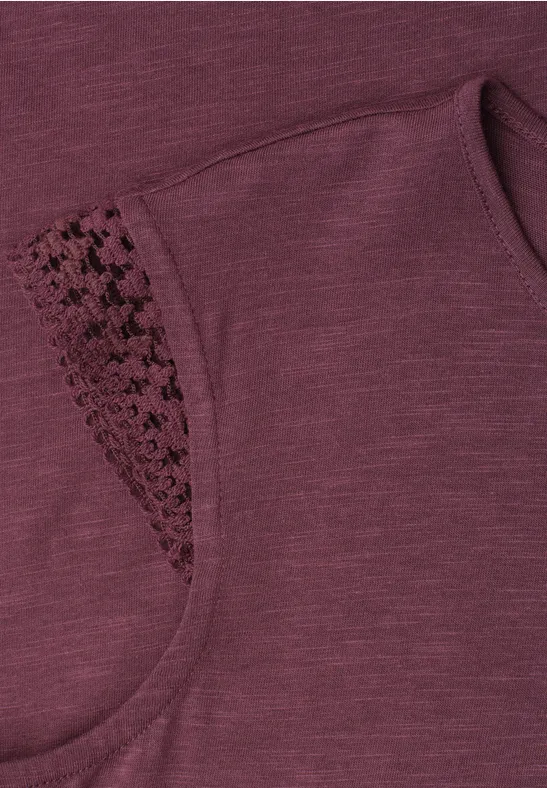 Close-up van een mouwloze donkerrode top met fijne kanten inzet aan de schouder.