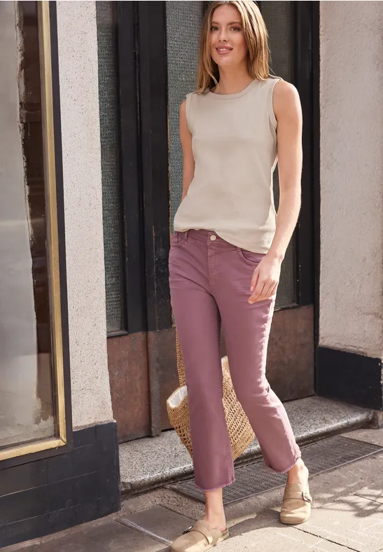 Kobieta w beżowym topie i różowych spodniach spaceruje po słonecznym chodniku przed elewacją.