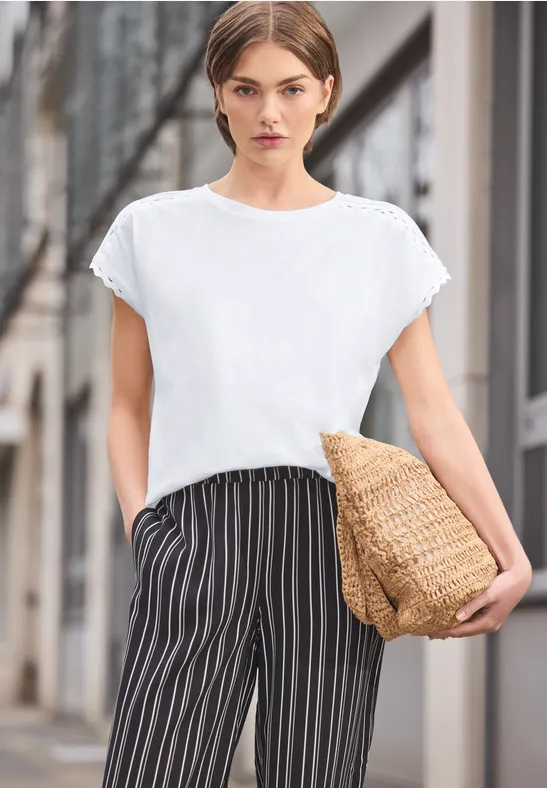 Vrouw in wit T-shirt, zwart-witte gestreepte broek met rieten tas op straat