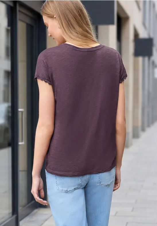 Junge Frau von hinten auf einem Bürgersteig, trägt dunkles T-Shirt und Jeans in urbaner Umgebung.