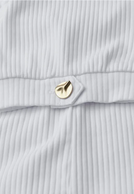 Nahaufnahme eines weißen, gerippten Stoffs mit einem kleinen goldenen Schmuckelement.