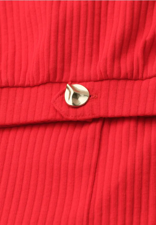 Nahaufnahme eines roten, gerippten Stoffs mit einem kleinen goldfarbenen Metallknopf