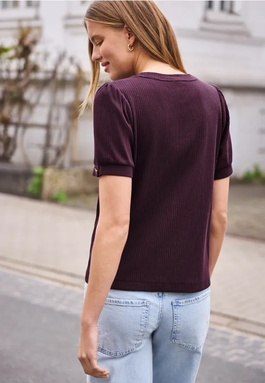 Een vrouw van achter gezien met een paars shirt en lichtblauwe spijkerbroek, lopend op een stoep in de stad.