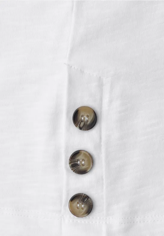 Nahaufnahme eines weißen Stoffes mit drei braunen Knöpfen in vertikaler Anordnung.