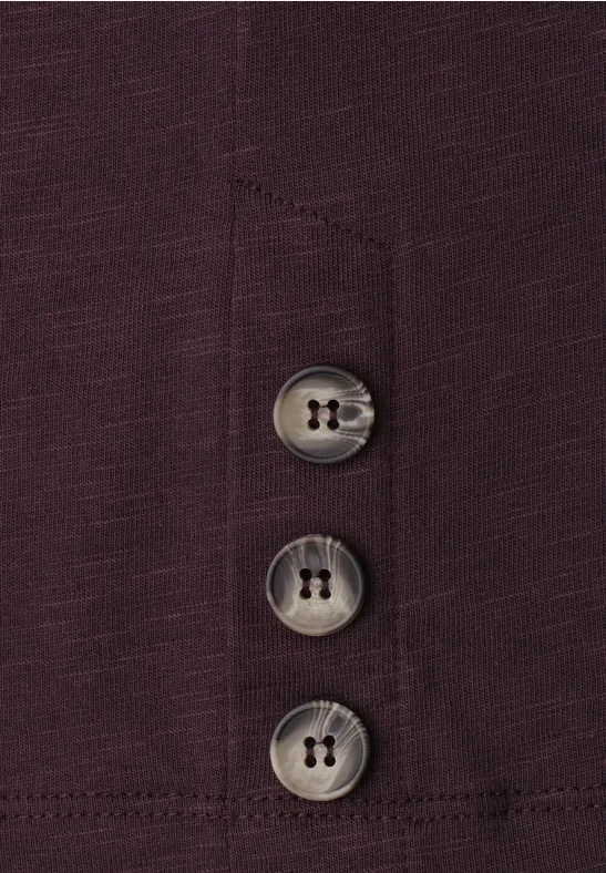 Dunkelviolettes Kleidungsstück mit drei grauen Knöpfen an einer Naht