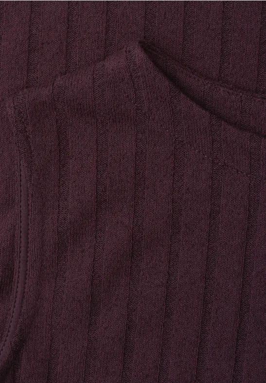 Nahaufnahme eines burgunderfarbenen, gerippten Strickstoffs mit angedeuteter Taschennaht.