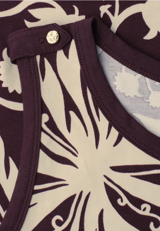 Gros plan d'un top violet et blanc à motif abstrait avec bouton métallique au col.