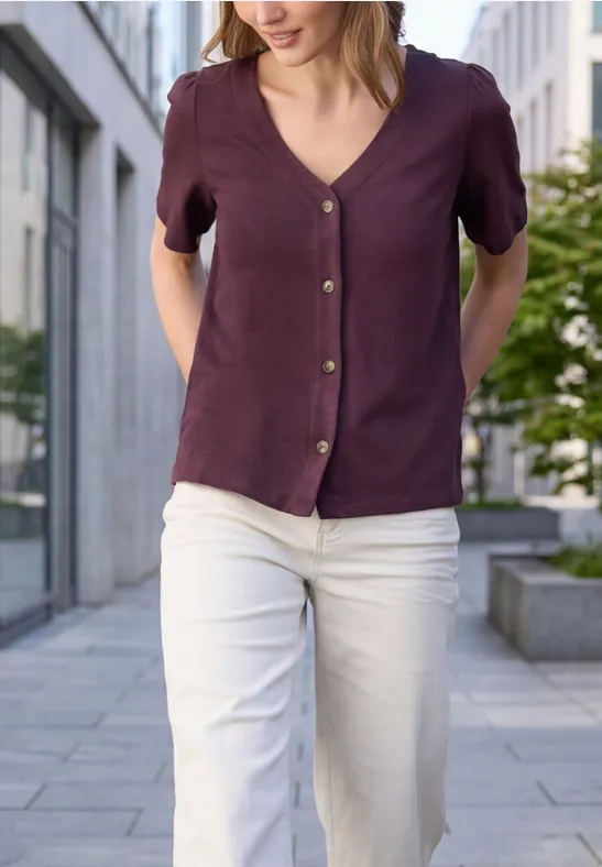 Eine Frau geht in weißer Hose und lila/blauer Bluse durch eine städtische Umgebung.