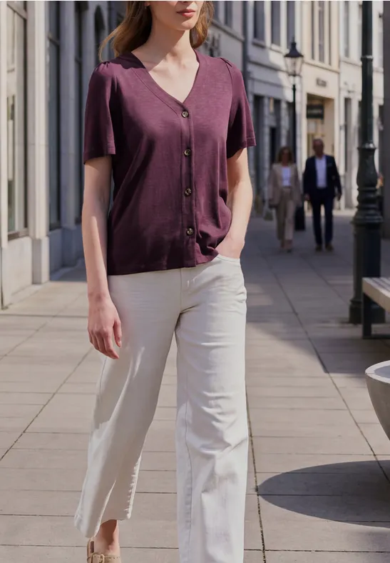 Eine Frau in lila Bluse und weißen Hosen geht in urbaner Umgebung spazieren.