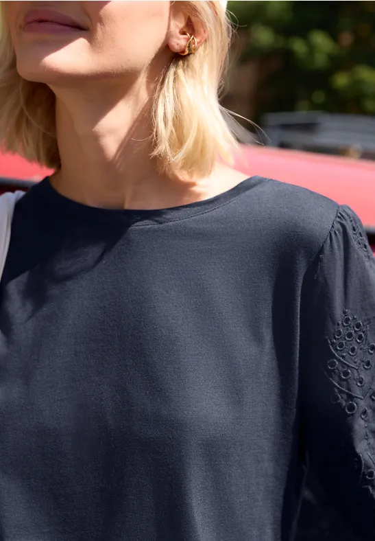 Halbportrait einer Frau mit blondem Haar in blauer Bluse, sitzend im Freien