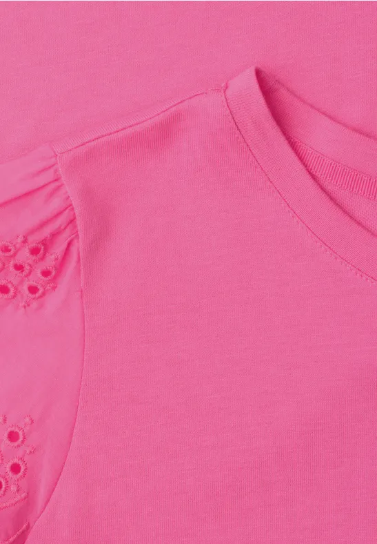 Nahaufnahme eines pinkfarbenen T-Shirts mit Rundhalsausschnitt und Spitzen-Lochstickerei an der Schulter.