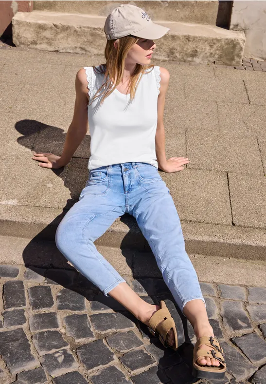 Jonge vrouw in jeans, wit topje en pet zit ontspannen op een opstapje buiten.