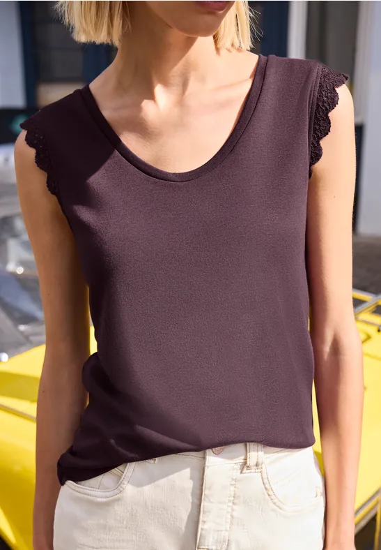 Vrouw draagt een donker mouwloos shirt en lichte broek voor een gele auto.