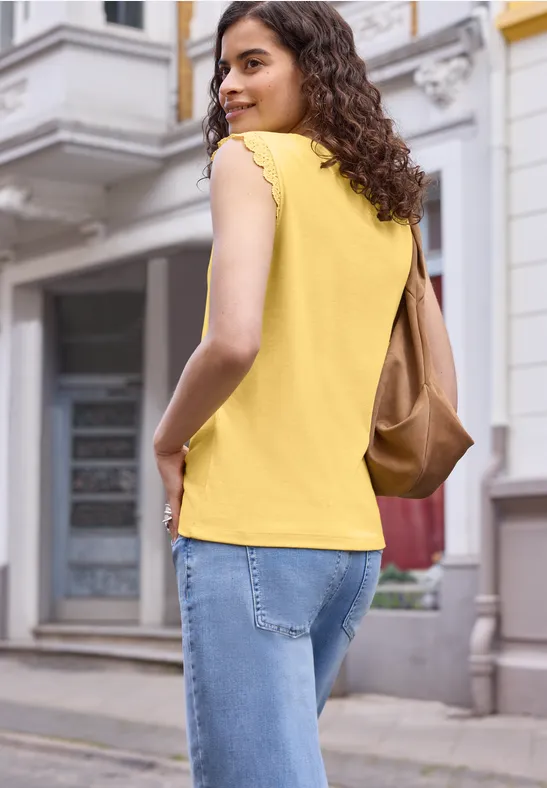 Frau in gelbem Top und Jeans mit brauner Tasche schlendert eine Straße entlang.