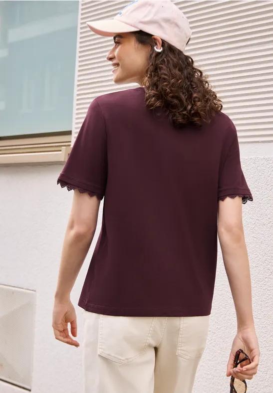 Frau von hinten mit weinrotem T-Shirt, beiger Hose, rosa Baseballcap und einer Sonnenbrille in der Hand.