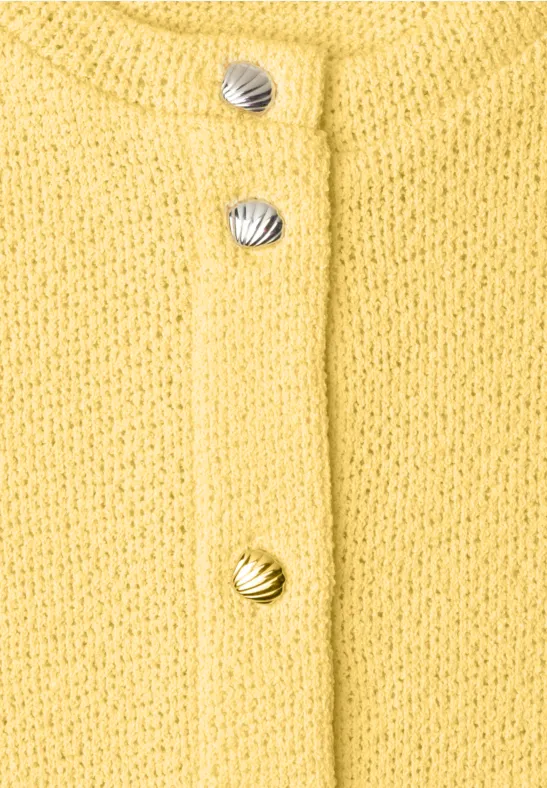 Nahaufnahme eines gelben Strickcardigans mit muschelförmigen Knöpfen in Silber und Gold.