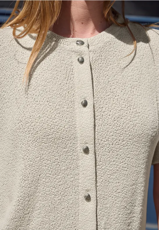 Person trägt cremefarbenen, strukturierten Cardigan mit Metallknöpfen.