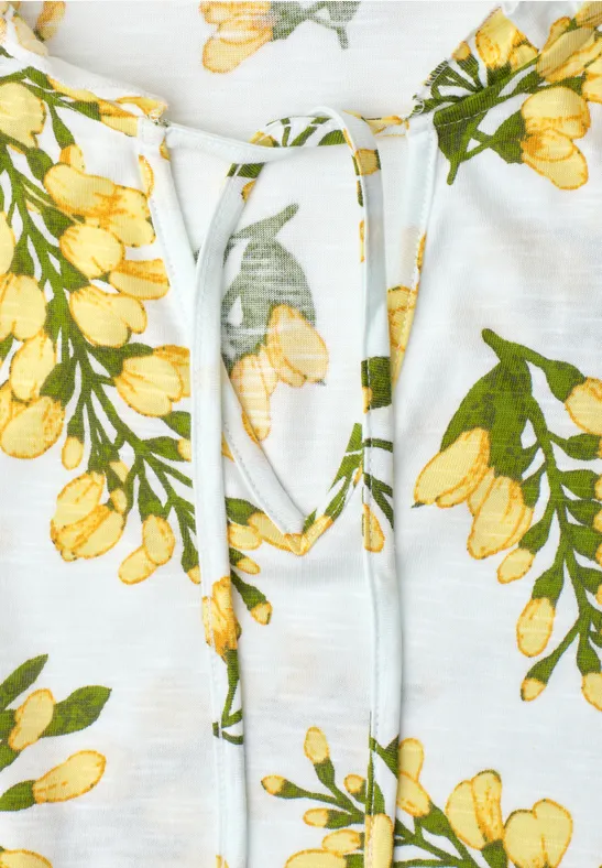 Witte top met gele bloemenprint en koordsluiting bij de hals.
