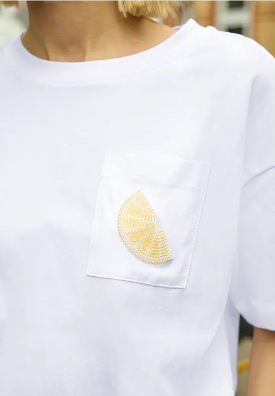 Weißes T-Shirt mit Brusttasche und gesticktem Zitronenschnitz.