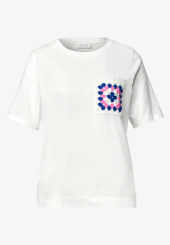 Weißes T-Shirt mit kurzem Arm und buntem geometrischem Muster auf der Brusttasche.