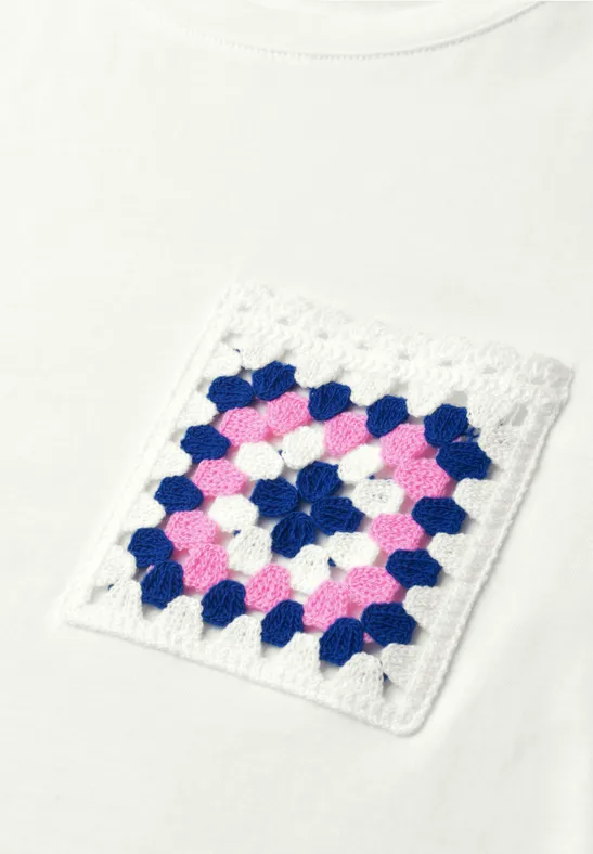 Weißes T-Shirt mit gehäkelter Tasche im Granny-Square-Muster in Pink, Blau und Weiß.