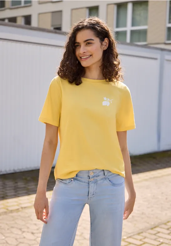 Eine Frau in gelbem T-Shirt und hellblauer Jeans steht vor Garagentoren.