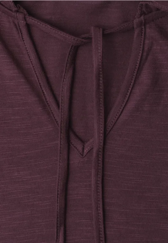 Close-up van een bordeaux hoodie met trekkoorden en fijne structuur.