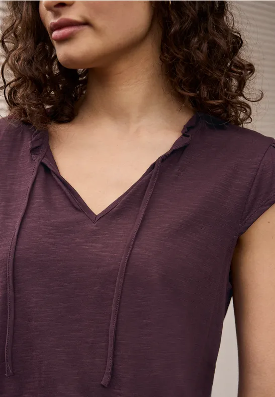 Een vrouw draagt een paars T-shirt met korte mouwen, V-hals en sierkoorden.