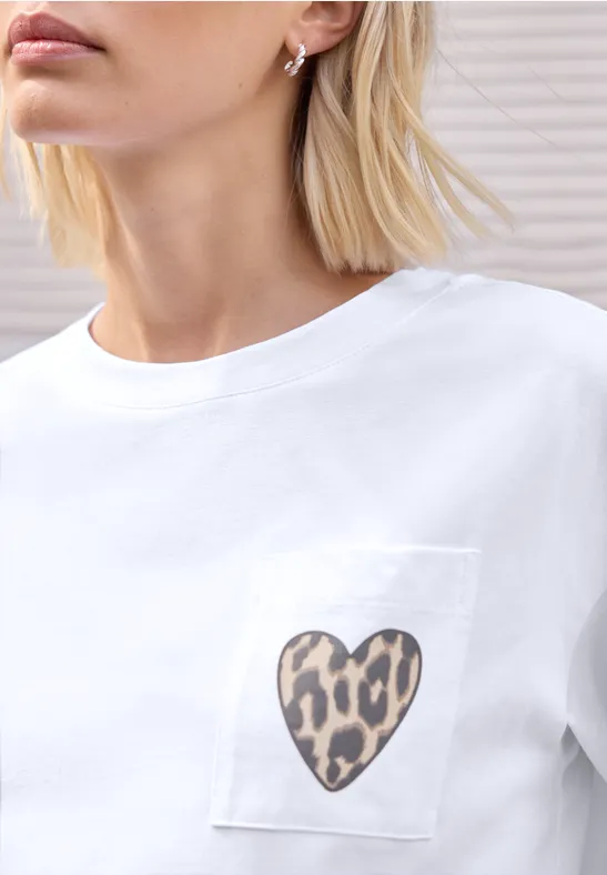 Weißes T-Shirt mit Brusttasche, darauf ein Herz im Leopardenmuster, getragen von Frau mit blondem Kurzhaar.