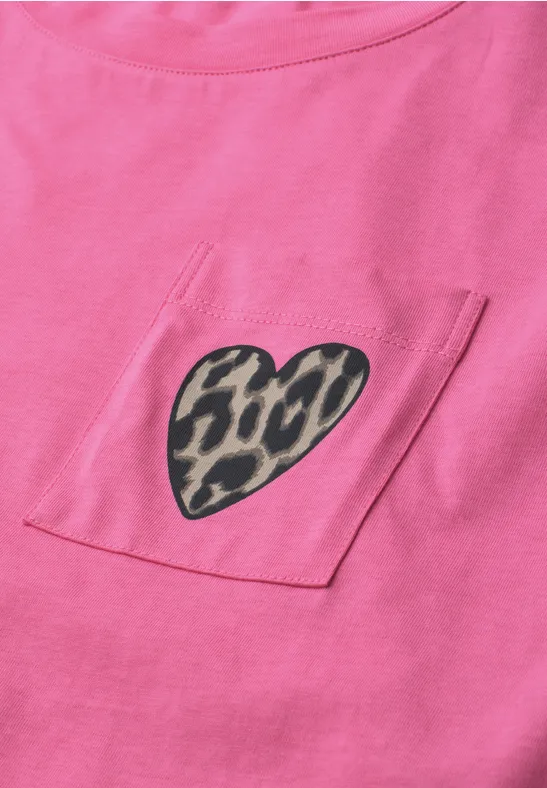 Nahaufnahme eines rosa T-Shirts mit einer Brusttasche, darauf ein Herz in Leopardenmuster.