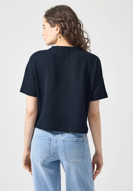 Eine von hinten gezeigte Frau trägt ein dunkelblaues Kurzarmshirt und helle Jeans.