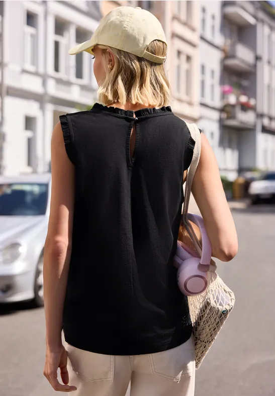 Person mit Baseballcap, schwarzem ärmellosem Top und Strohtasche geht eine Straße entlang.