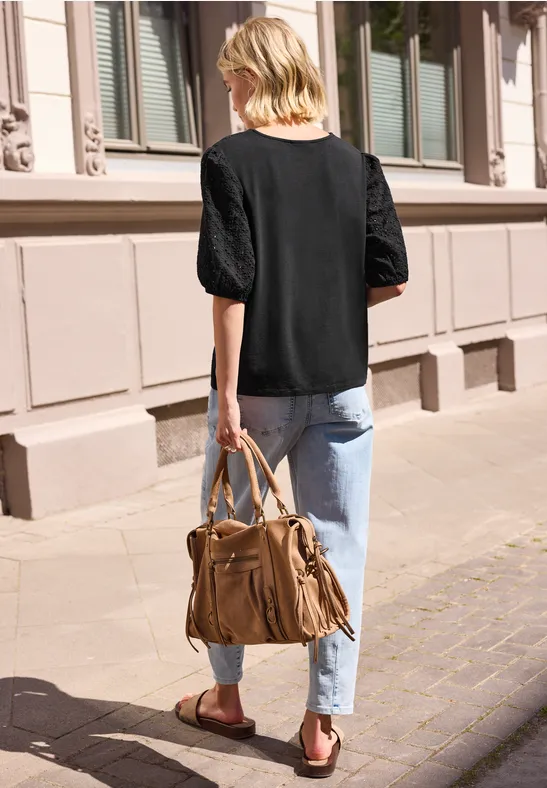 Rückansicht einer Frau in schwarzer Bluse und Jeans, die mit einer großen braunen Tasche auf dem Bürgersteig spaziert.