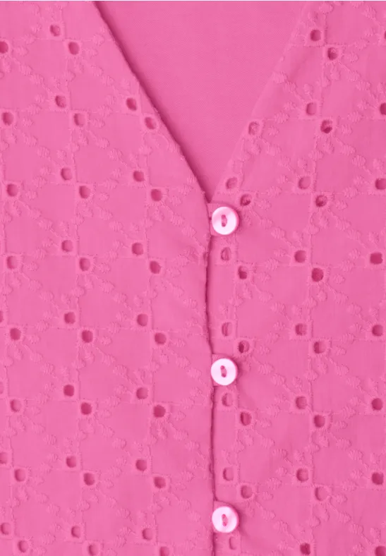 Close-up van een roze top met ajourborduurwerk en kleine knoopjes langs de V-hals.