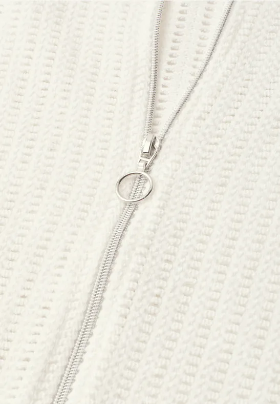 Close-up van een crèmekleurige gebreide trui met een centrale rits en een ronde ritsklink.