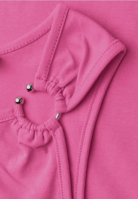 Close-up van roze stof met twee geplooide cirkels, verbonden door kleine zilverkleurige kraaltjes.