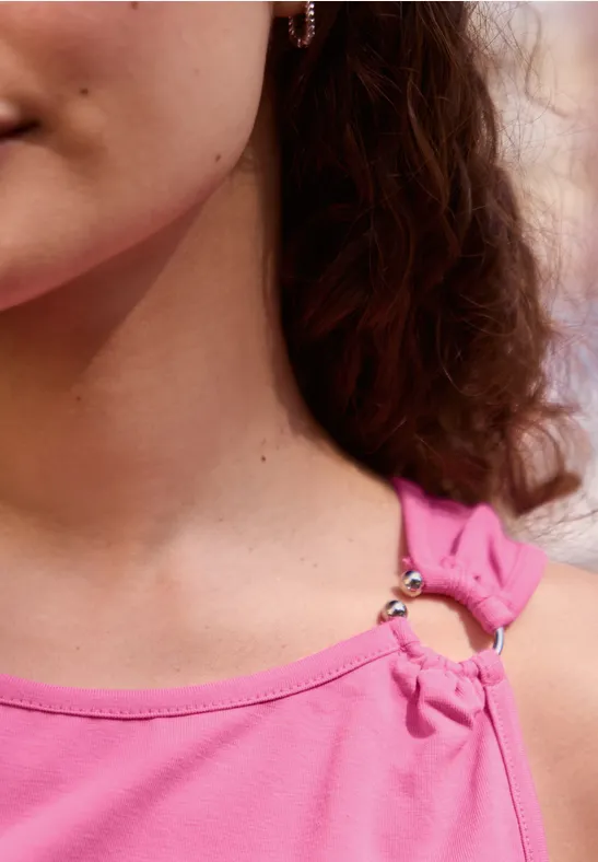 Close-up van de hals en schouder van een vrouw met krullend haar en een roze top met ringdetail.