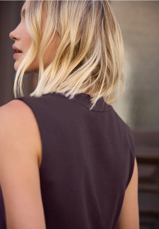Seitliche Ansicht einer Frau mit schulterlangen blonden Haaren und schwarzem ärmellosem Top.